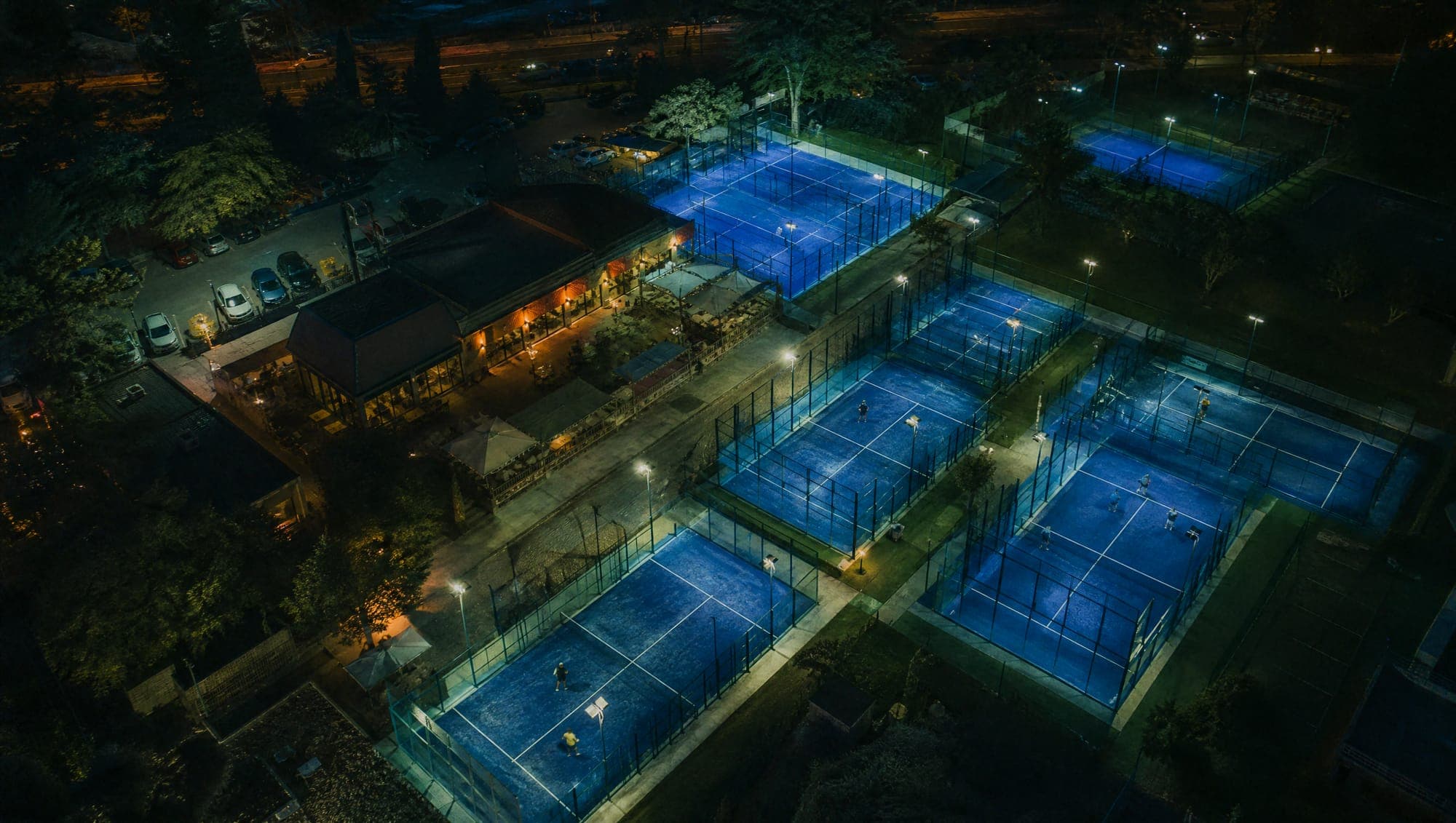 Club de pádel con varias canchas iluminadas, vista aérea de noche